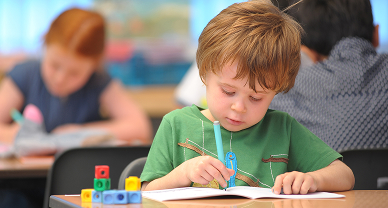 A young boy writing at a desk in a classroom.